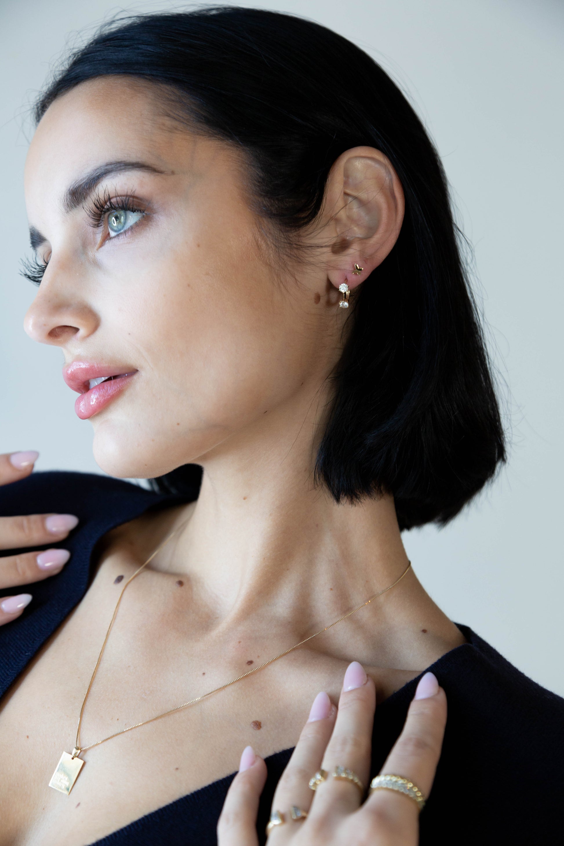 Woman wearing gold jewelry including earrings, necklace, and rings against a neutral background