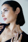 Woman wearing gold jewelry including earrings, necklace, and rings against a neutral background